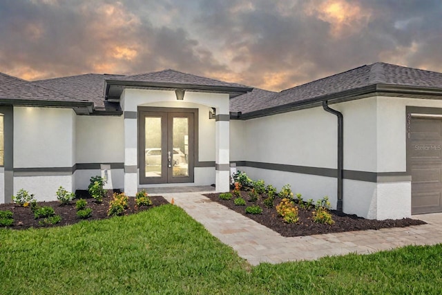 exterior entry at dusk featuring a lawn, a garage, and french doors