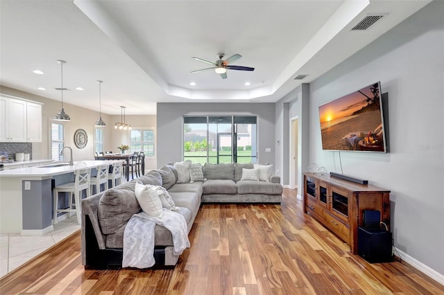 living room featuring a raised ceiling, ceiling fan, sink, and light hardwood / wood-style floors