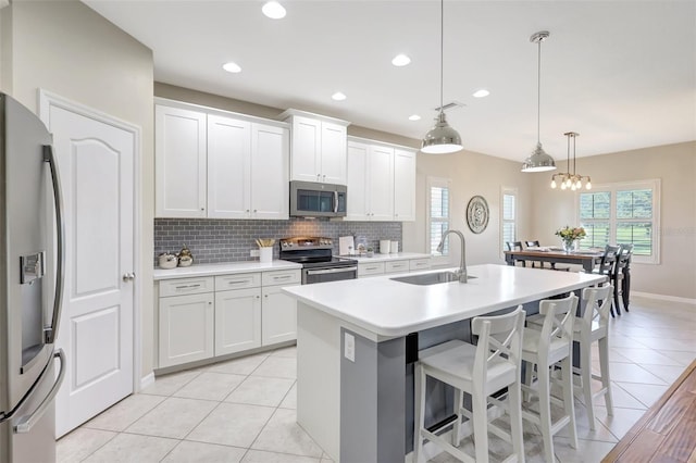 kitchen featuring white cabinetry, sink, stainless steel appliances, pendant lighting, and a kitchen island with sink