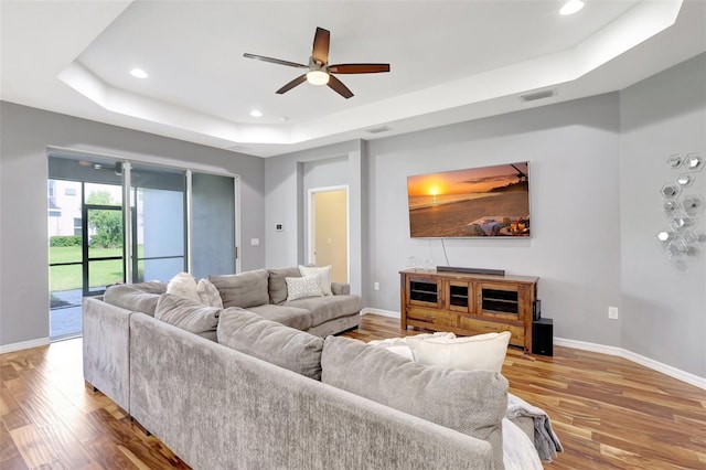 living room featuring hardwood / wood-style floors, a tray ceiling, and ceiling fan