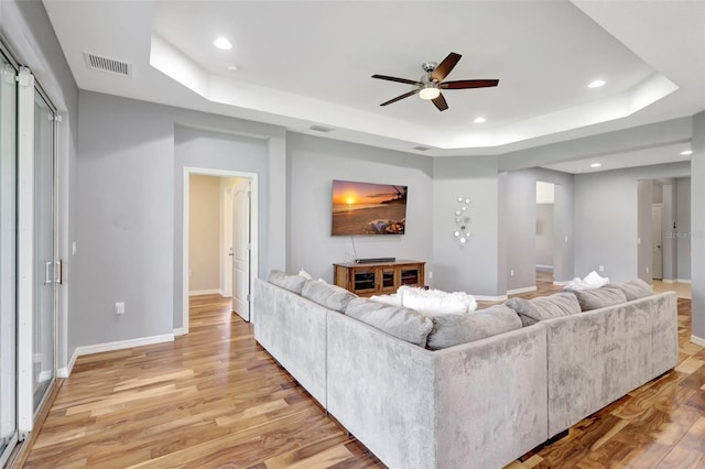 living room featuring ceiling fan, light wood-type flooring, and a tray ceiling