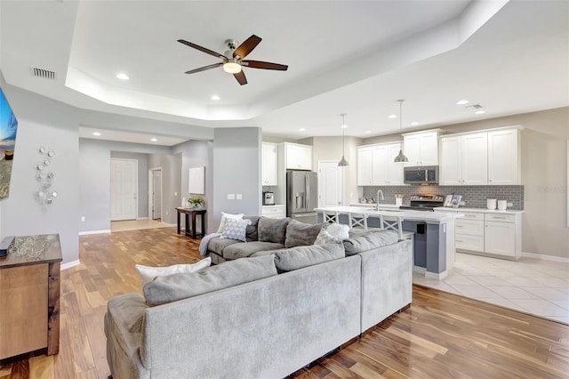 living room featuring light wood-type flooring, a tray ceiling, and ceiling fan