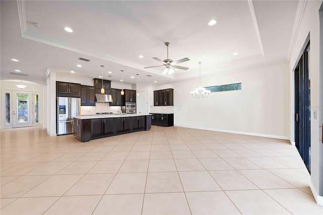 kitchen with a tray ceiling, stainless steel fridge, an island with sink, and exhaust hood