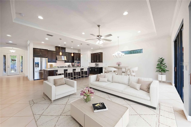 living room with ceiling fan with notable chandelier, light tile patterned flooring, ornamental molding, and a tray ceiling