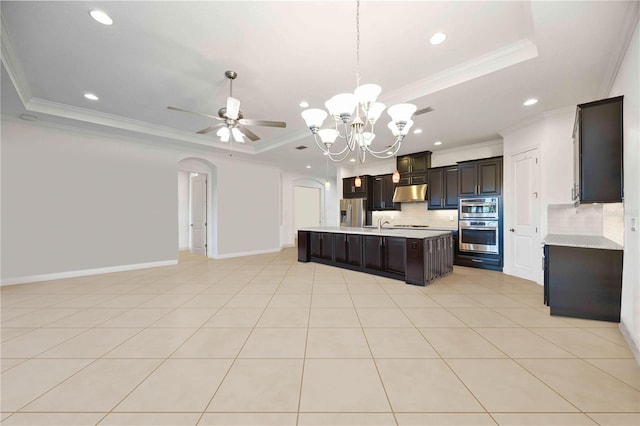 kitchen with backsplash, a center island with sink, crown molding, a tray ceiling, and light tile patterned flooring