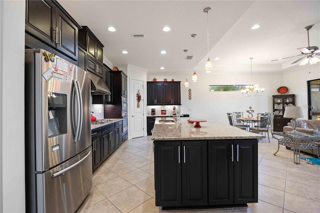 kitchen featuring hanging light fixtures, decorative backsplash, an island with sink, appliances with stainless steel finishes, and light stone counters