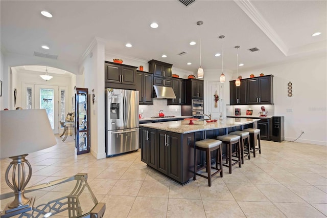 kitchen with decorative backsplash, light tile patterned floors, an island with sink, appliances with stainless steel finishes, and decorative light fixtures