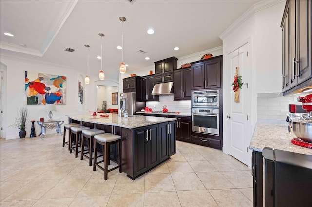 kitchen featuring backsplash, a kitchen island with sink, hanging light fixtures, ornamental molding, and a breakfast bar area