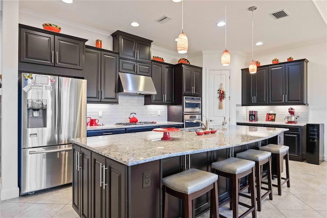 kitchen featuring pendant lighting, light tile patterned floors, a kitchen island with sink, and appliances with stainless steel finishes