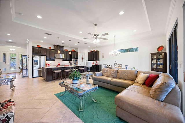 living room featuring light tile patterned floors, ceiling fan with notable chandelier, a raised ceiling, and ornamental molding