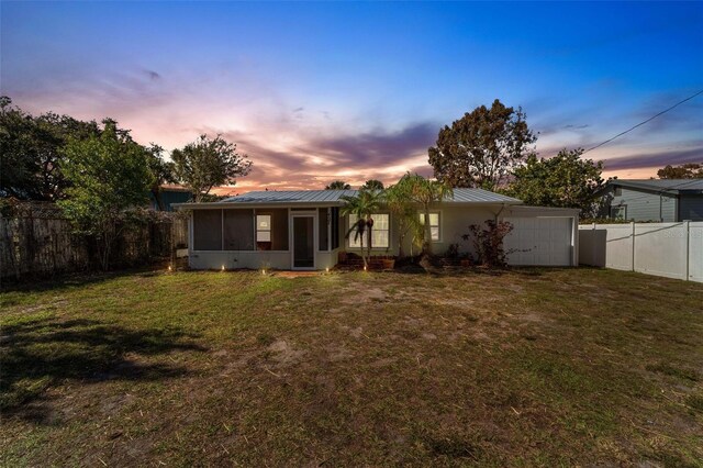 back house at dusk with a sunroom, a garage, and a yard