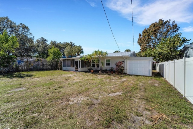 rear view of property featuring a sunroom, a yard, and a garage