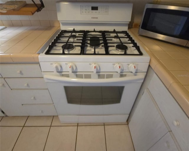 room details featuring tile countertops, white cabinetry, and white gas stove