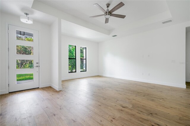 empty room featuring light wood-type flooring, ceiling fan, and a raised ceiling