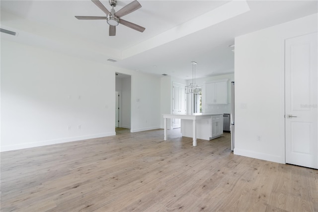 unfurnished living room with ceiling fan with notable chandelier, a tray ceiling, and light hardwood / wood-style floors