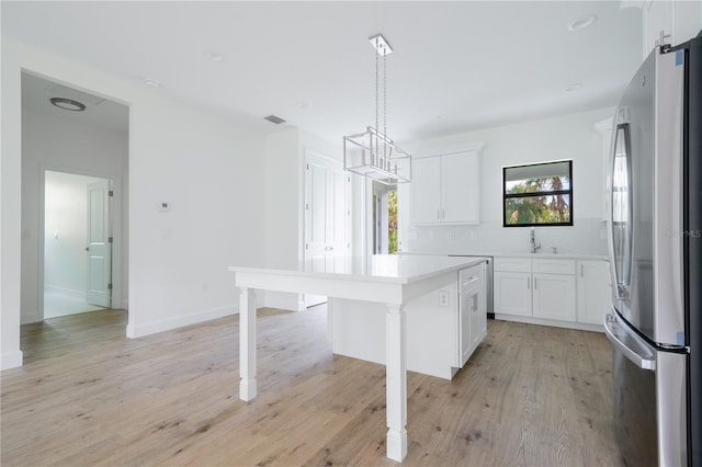 kitchen with a kitchen island, freestanding refrigerator, light countertops, white cabinetry, and pendant lighting