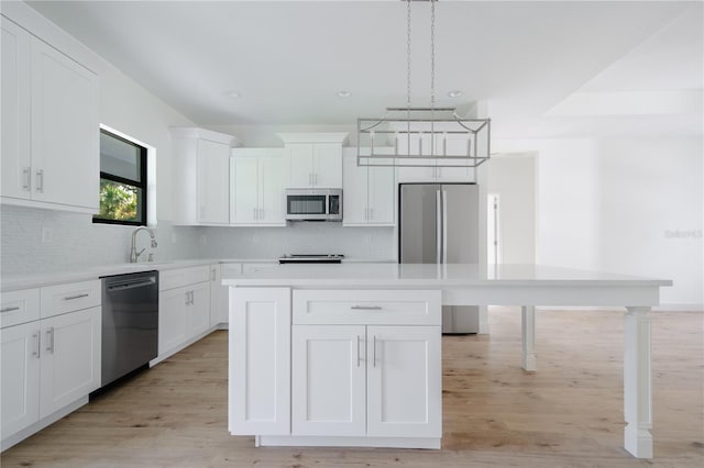 kitchen with stainless steel appliances, a kitchen island, light countertops, and white cabinets