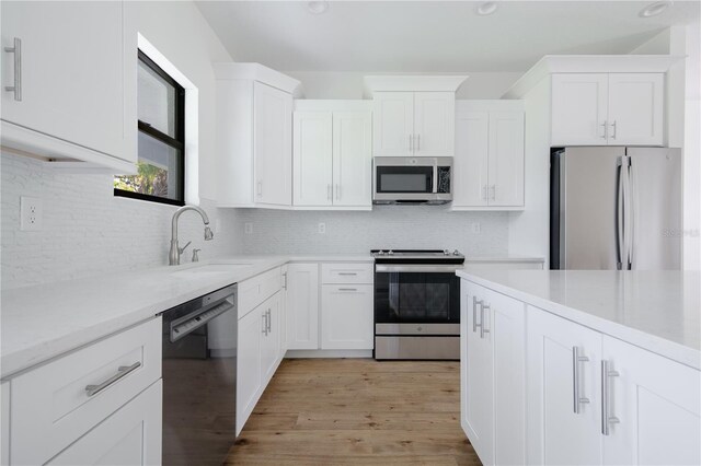 kitchen featuring white cabinets, a sink, stainless steel appliances, light wood-style floors, and backsplash