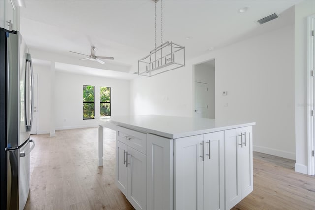 kitchen with a kitchen island, visible vents, white cabinets, light countertops, and freestanding refrigerator