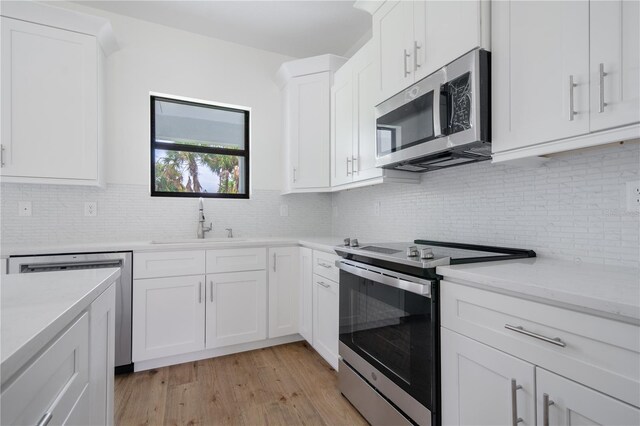 kitchen with light wood-type flooring, white cabinetry, backsplash, stainless steel appliances, and sink