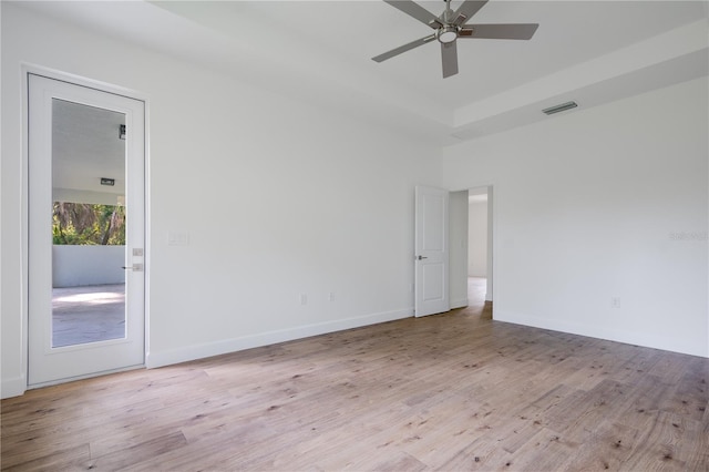 empty room with visible vents, light wood finished floors, a ceiling fan, and baseboards