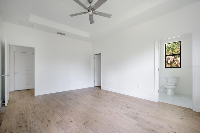 unfurnished bedroom with light wood finished floors, baseboards, visible vents, and a raised ceiling