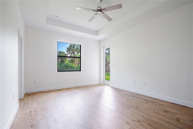 empty room featuring light wood-type flooring, a raised ceiling, ceiling fan, and baseboards