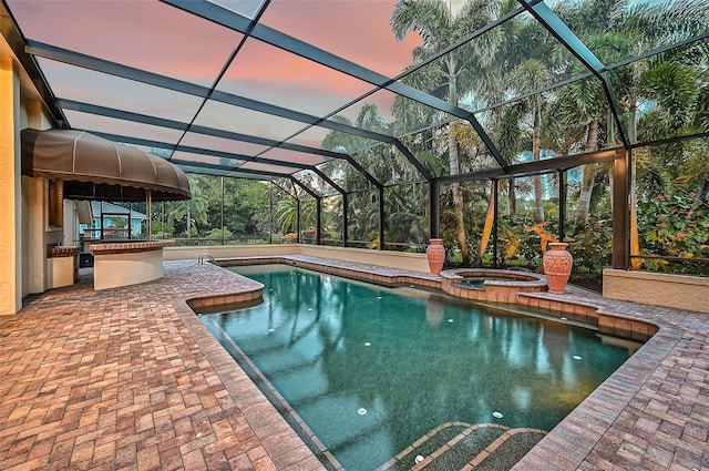 pool at dusk featuring glass enclosure, an in ground hot tub, and a patio