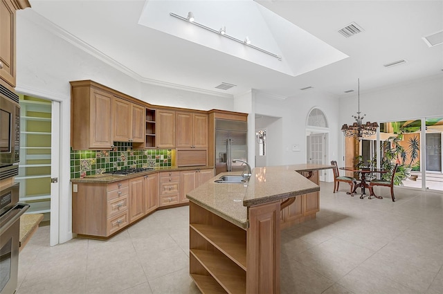 kitchen with ornamental molding, a chandelier, sink, appliances with stainless steel finishes, and a center island with sink