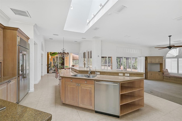 kitchen with ceiling fan with notable chandelier, a skylight, stainless steel appliances, sink, and an island with sink