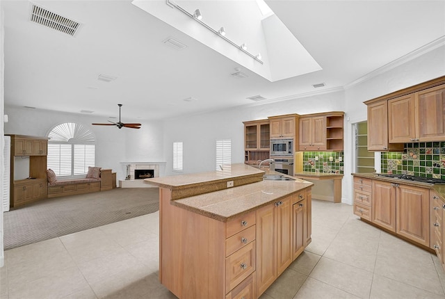 kitchen featuring backsplash, a kitchen island with sink, stainless steel appliances, sink, and ceiling fan