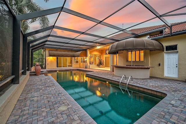 pool at dusk with glass enclosure and a patio area