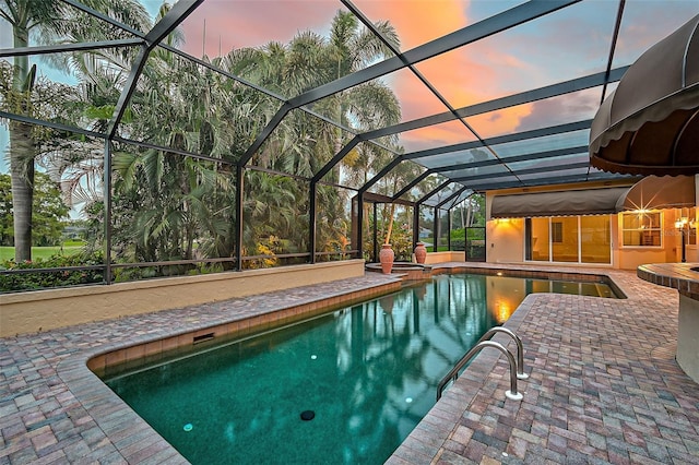 pool at dusk featuring glass enclosure and a patio