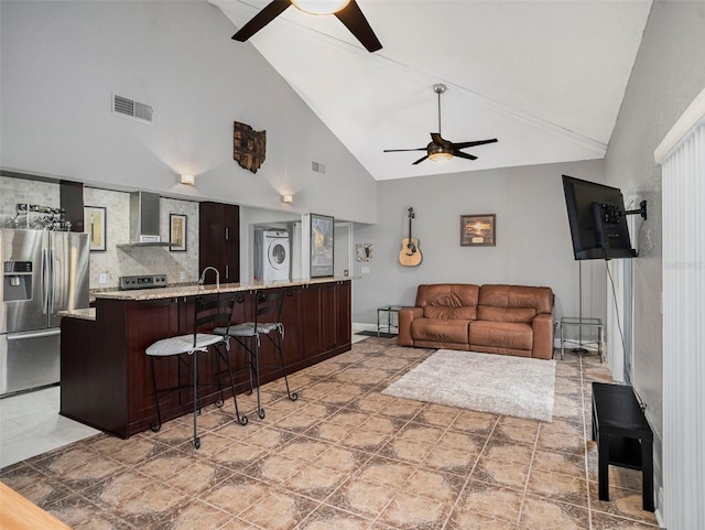 tiled living room featuring stacked washer / dryer, high vaulted ceiling, sink, and ceiling fan