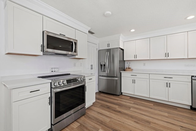 kitchen featuring recessed lighting, stainless steel appliances, white cabinetry, light wood-type flooring, and crown molding