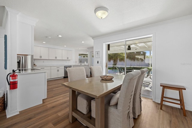 dining space featuring wood-type flooring, ceiling fan, crown molding, and a textured ceiling