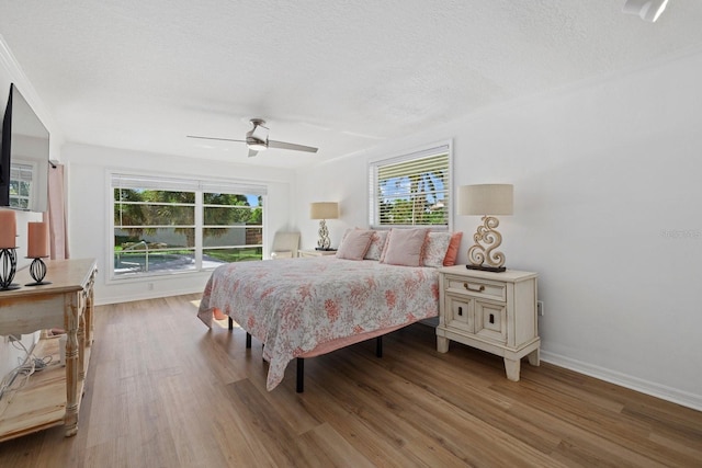 bedroom with a ceiling fan, a textured ceiling, baseboards, and wood finished floors