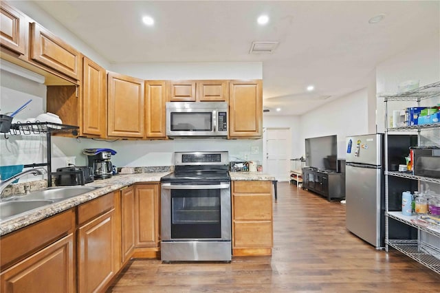 kitchen featuring appliances with stainless steel finishes, hardwood / wood-style flooring, light stone countertops, and sink