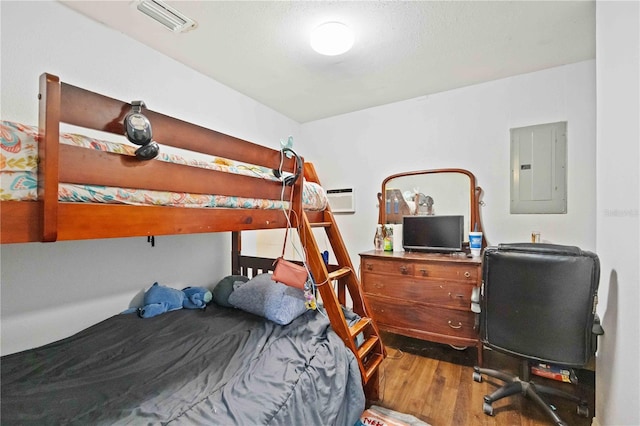 bedroom featuring electric panel, a wall mounted AC, and hardwood / wood-style floors