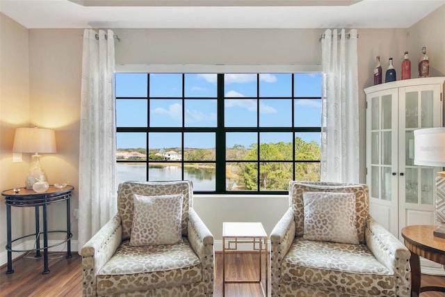 sitting room featuring a water view, baseboards, and wood finished floors