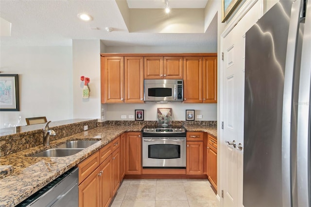 kitchen featuring dark stone counters, brown cabinets, stainless steel appliances, a sink, and light tile patterned flooring