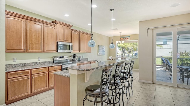 kitchen featuring a breakfast bar area, light stone countertops, pendant lighting, appliances with stainless steel finishes, and a kitchen island with sink