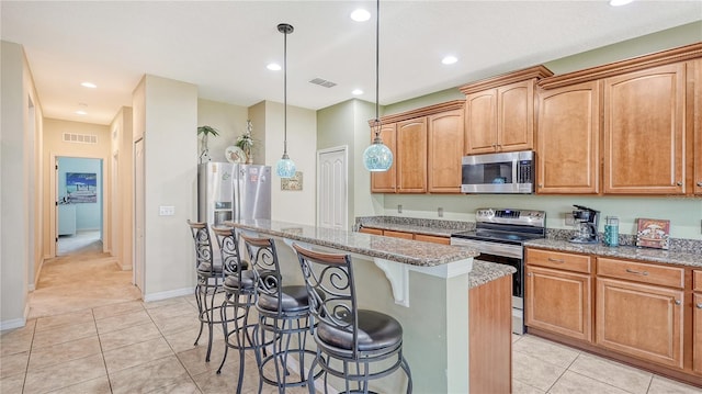 kitchen featuring hanging light fixtures, light stone counters, stainless steel appliances, a kitchen breakfast bar, and a kitchen island