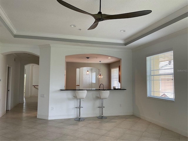 kitchen with ornamental molding, a breakfast bar area, dark countertops, and a raised ceiling