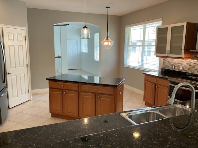 kitchen with backsplash, light tile patterned floors, dark stone countertops, sink, and pendant lighting