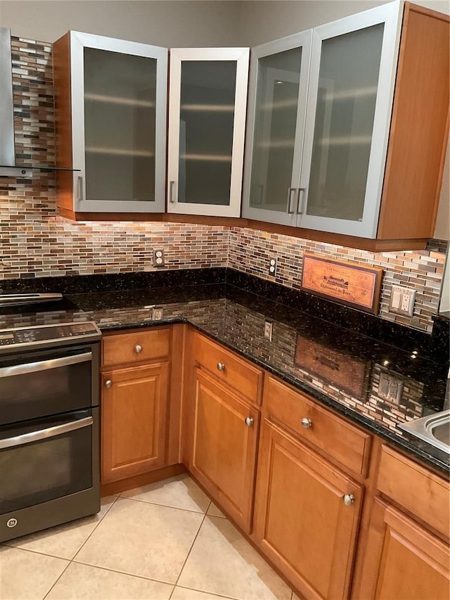 kitchen featuring range with two ovens, dark stone countertops, backsplash, and light tile patterned flooring