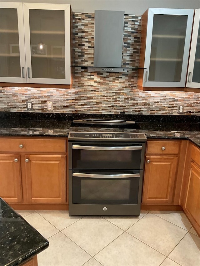 kitchen featuring wall chimney range hood, decorative backsplash, stainless steel gas range, and light tile patterned flooring