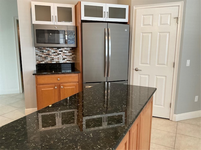 kitchen featuring light tile patterned floors, appliances with stainless steel finishes, glass insert cabinets, and tasteful backsplash