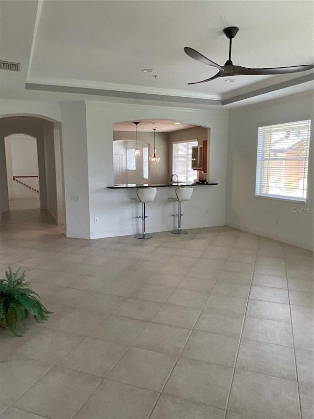 unfurnished living room with tile patterned flooring, ceiling fan, and a tray ceiling