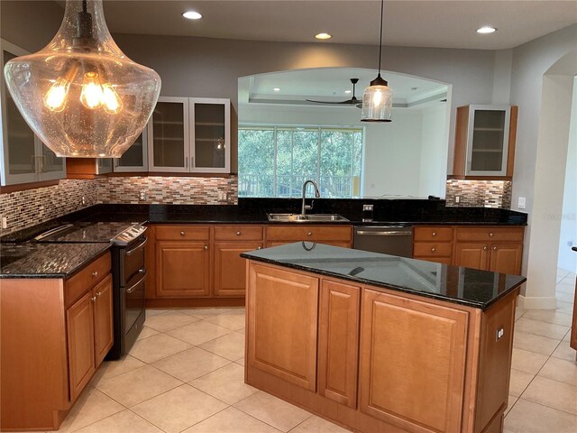 kitchen featuring a center island, appliances with stainless steel finishes, glass insert cabinets, a sink, and dark stone countertops